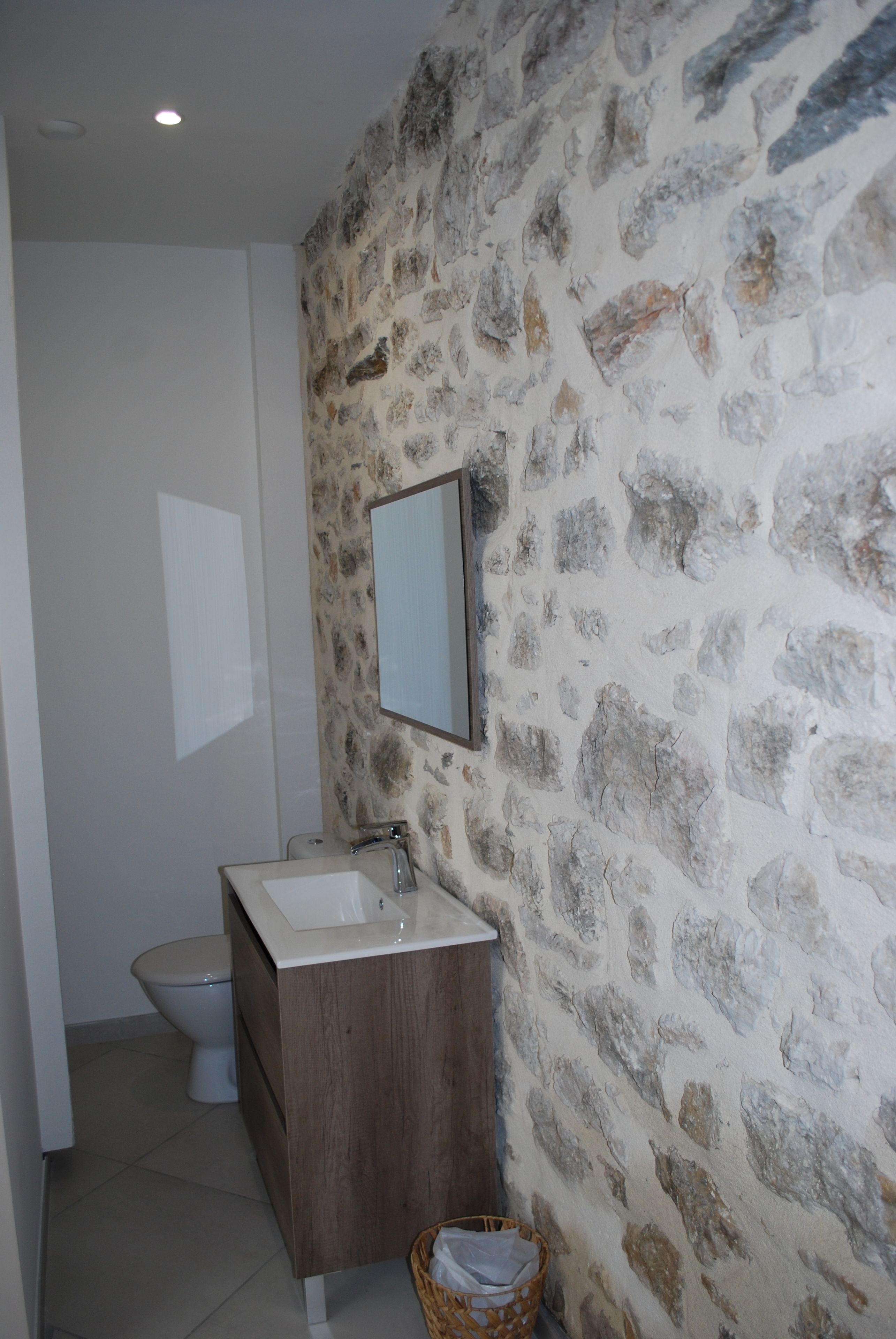 Un baño con pared de piedra, tocador de madera, lavamanos y inodoro.