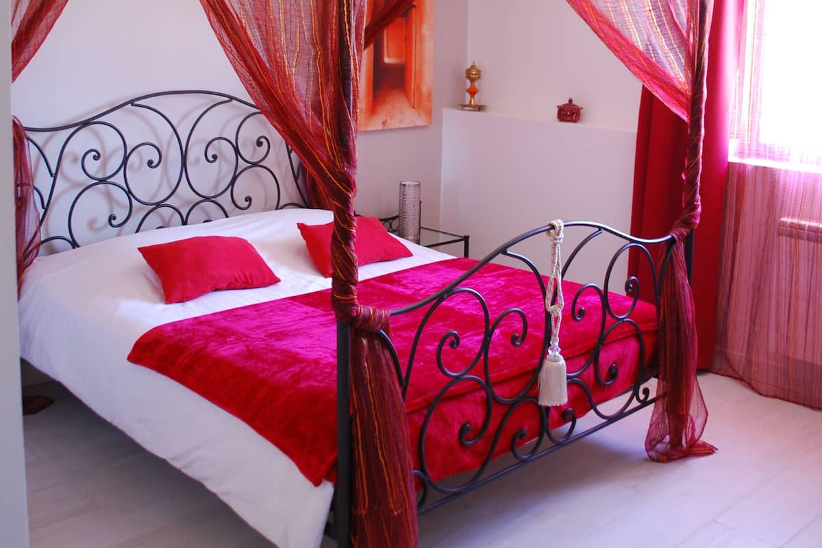 Una cama con dosel, ropa de cama roja y una pared blanca.