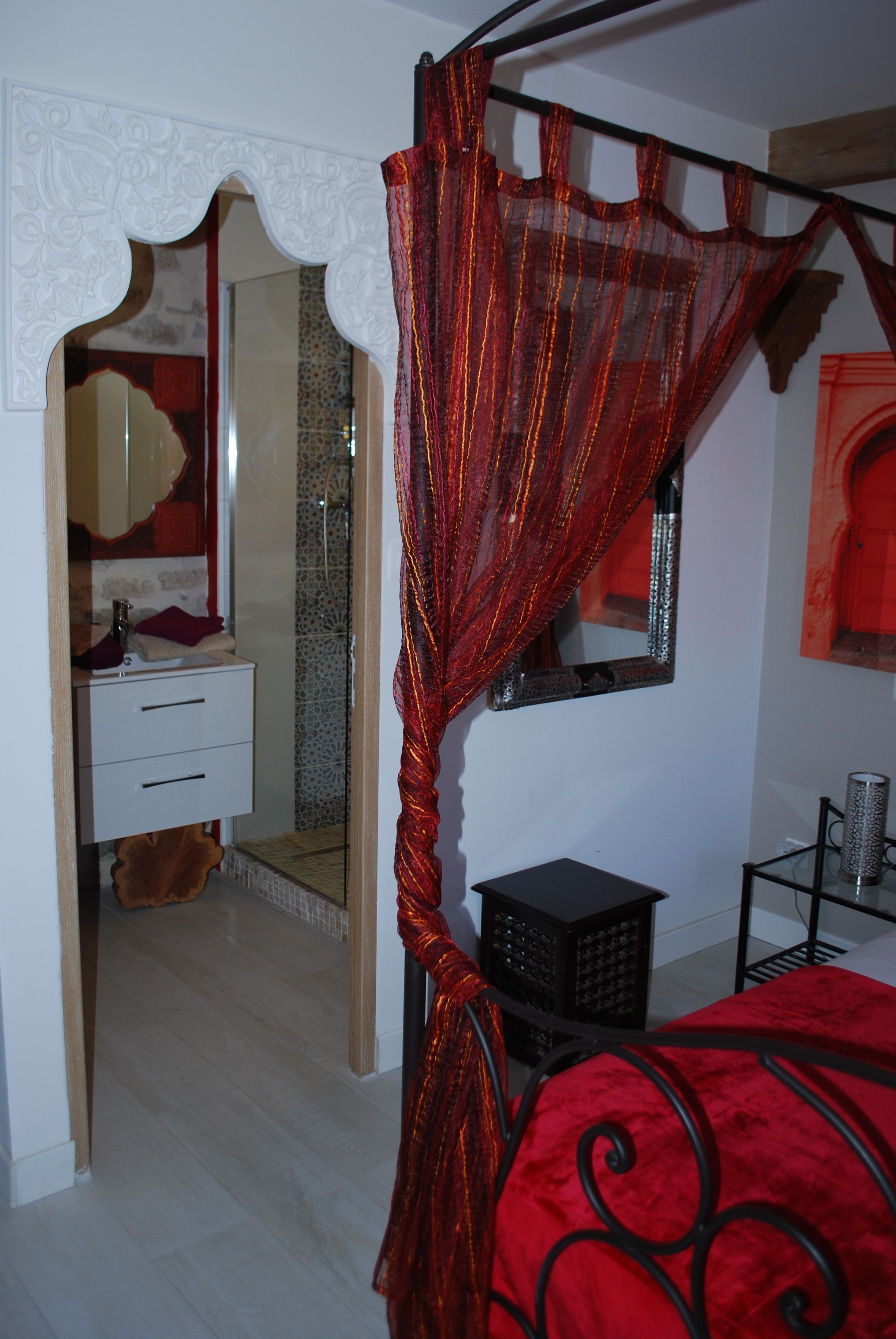 Un dormitorio con cama, dosel rojo, espejo, tocador y zona de ducha.