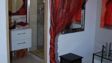Un dormitorio con cama, dosel rojo, espejo, tocador y zona de ducha.