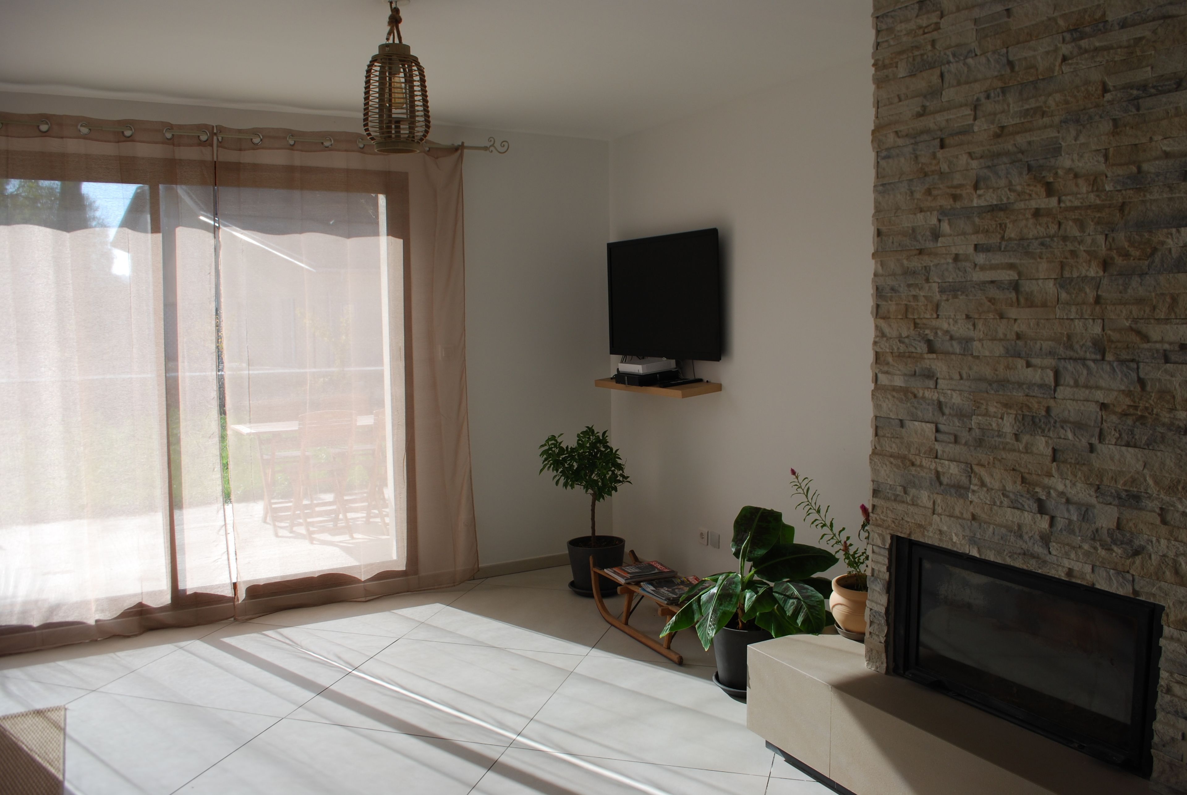 Un salon avec un mur en pierre, un téléviseur à écran plat fixé au mur, une cheminée et une porte-fenêtre coulissante donnant sur un espace extérieur.