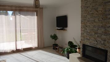 Un salon avec un mur en pierre, un téléviseur à écran plat fixé au mur, une cheminée et une porte-fenêtre coulissante donnant sur un espace extérieur.