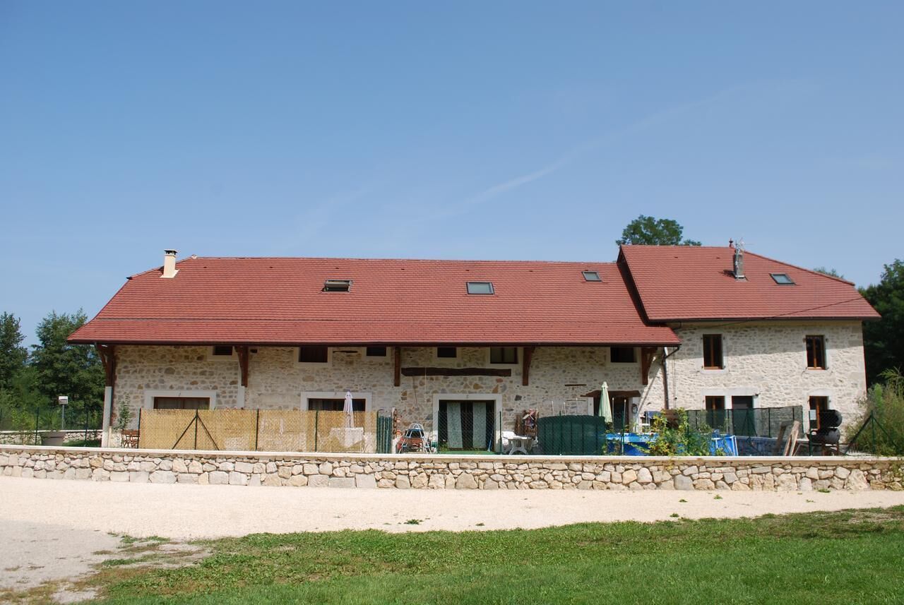 Un bâtiment en pierre à deux étages, avec un toit rouge, un mur de pierre à l’avant et un ciel dégagé.