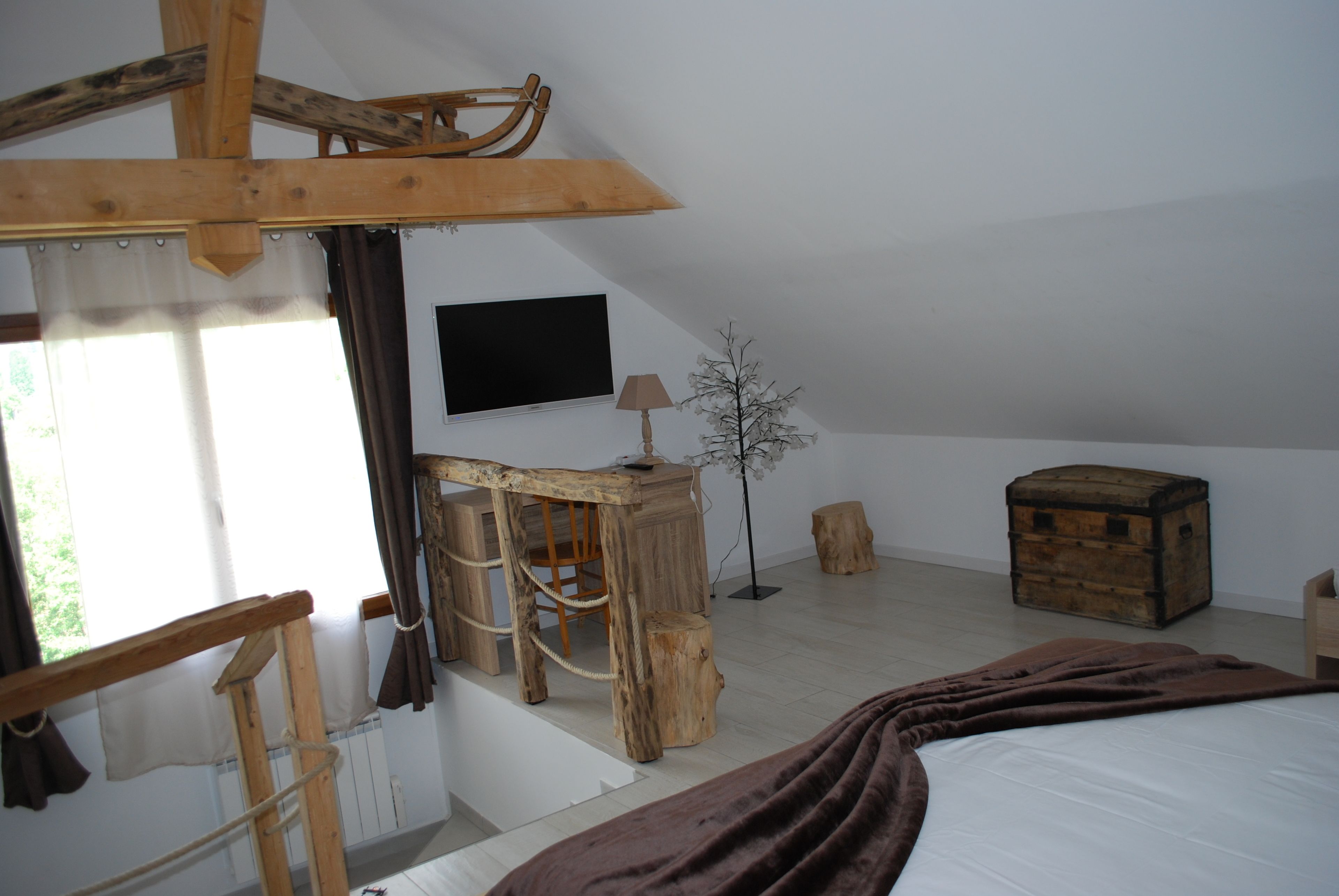 Une chambre rustique avec un lit, des meubles en bois, une télévision et une fenêtre avec des rideaux.