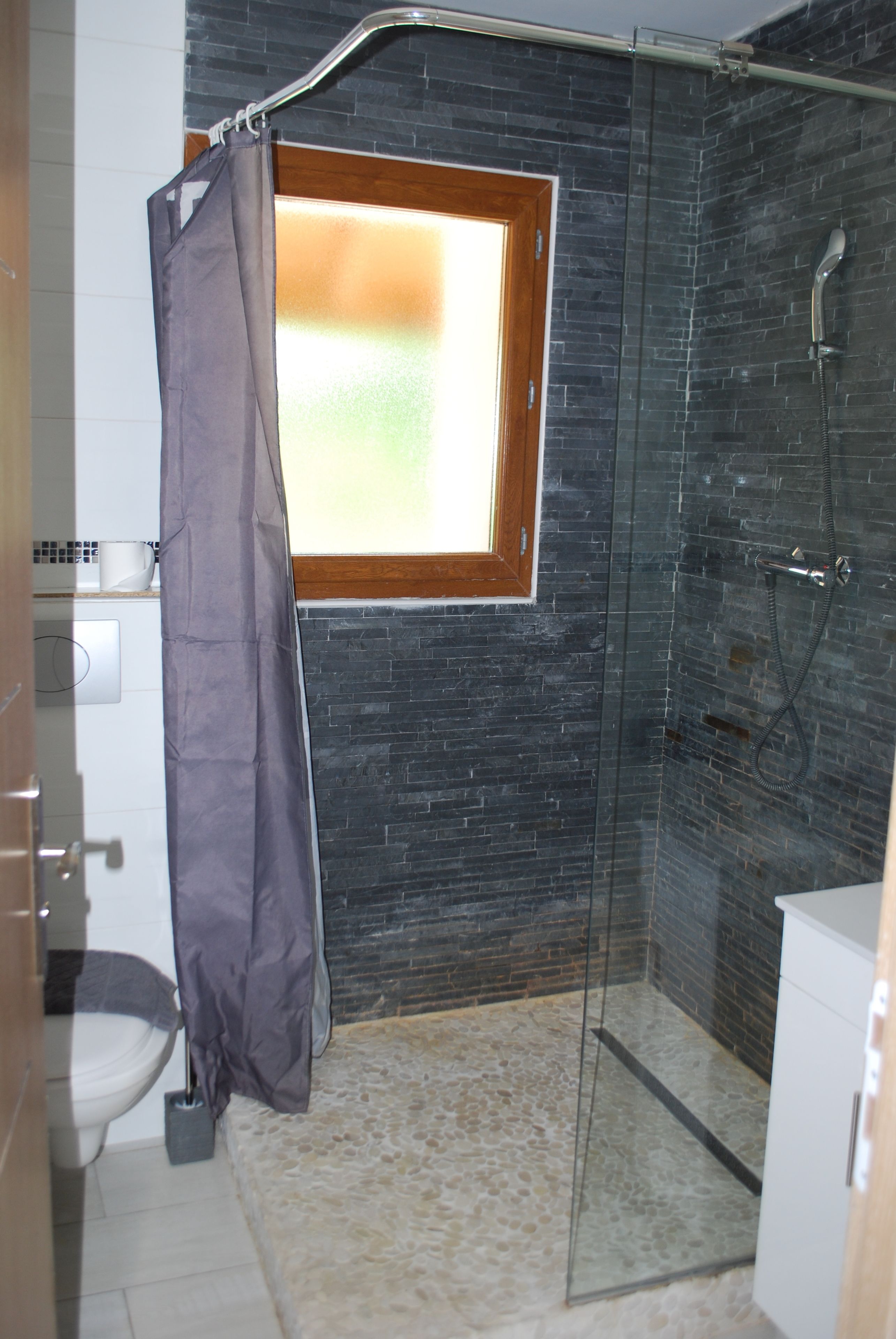 Et badeværelse med bruser, et vindue og et toilet.