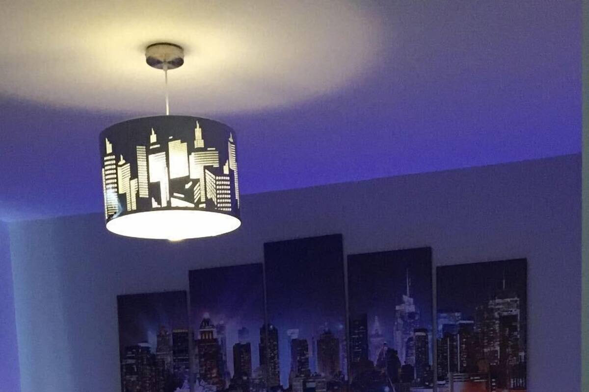 Un dormitorio moderno con un mural de la ciudad, una cama con cabecera iluminada en azul y una iluminación ambiental.