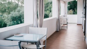 Un balcon avec une table et des chaises en verre, des rideaux et une vue sur la verdure.