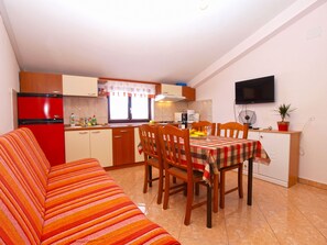 A compact kitchen with a dining area, a sofa, and a TV mounted on the wall.