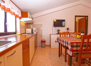 A compact kitchen with a dining area, a TV mounted on the wall, and a trash bin.