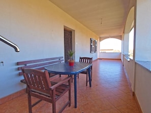 A balcony with a table and chairs, a potted plant, and a window with blinds.