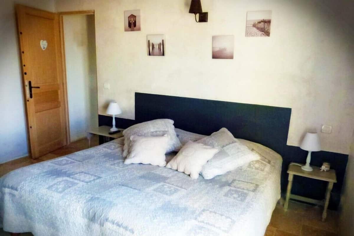 A bedroom with a bed, pillows, a nightstand, a lamp, and a door.