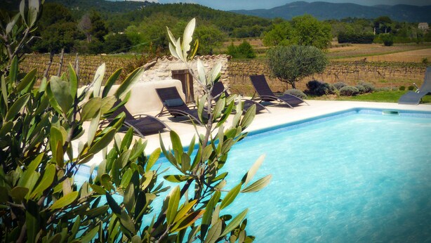 Zona de piscina con sillas de descanso, un edificio de piedra y un viñedo al fondo.