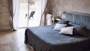 Un dormitorio con una cama grande, una mesita pequeña y una silla cerca de un ventanal corredizo.