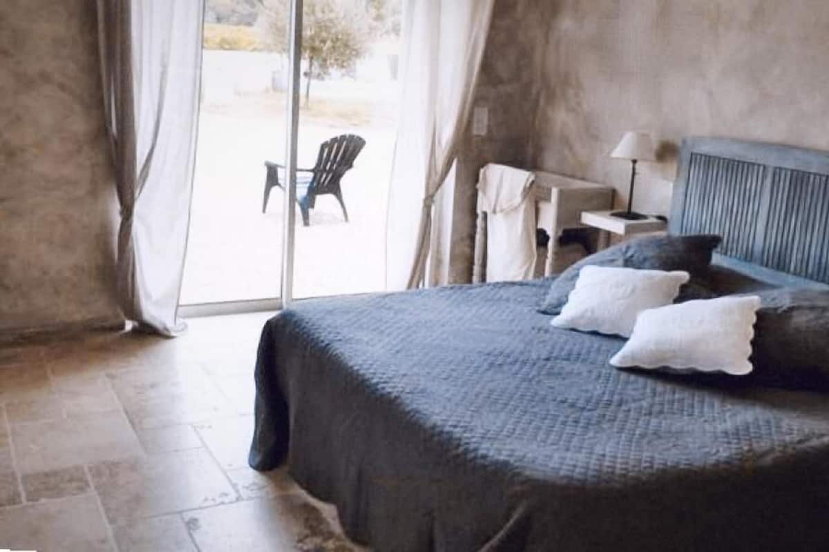 A bedroom with a large bed, a small table, and a chair near a sliding glass door.