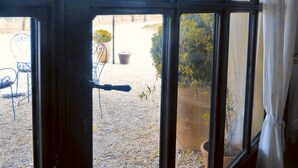 Vista por una ventana con una silla de metal y plantas en macetas afuera.