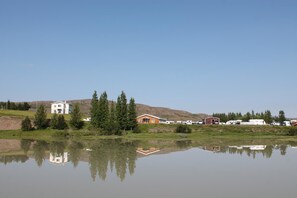 A lakeside property with a white house, a red barn, and several RVs parked nearby. - Skipalækur Guesthouse (Egilsstaðir)