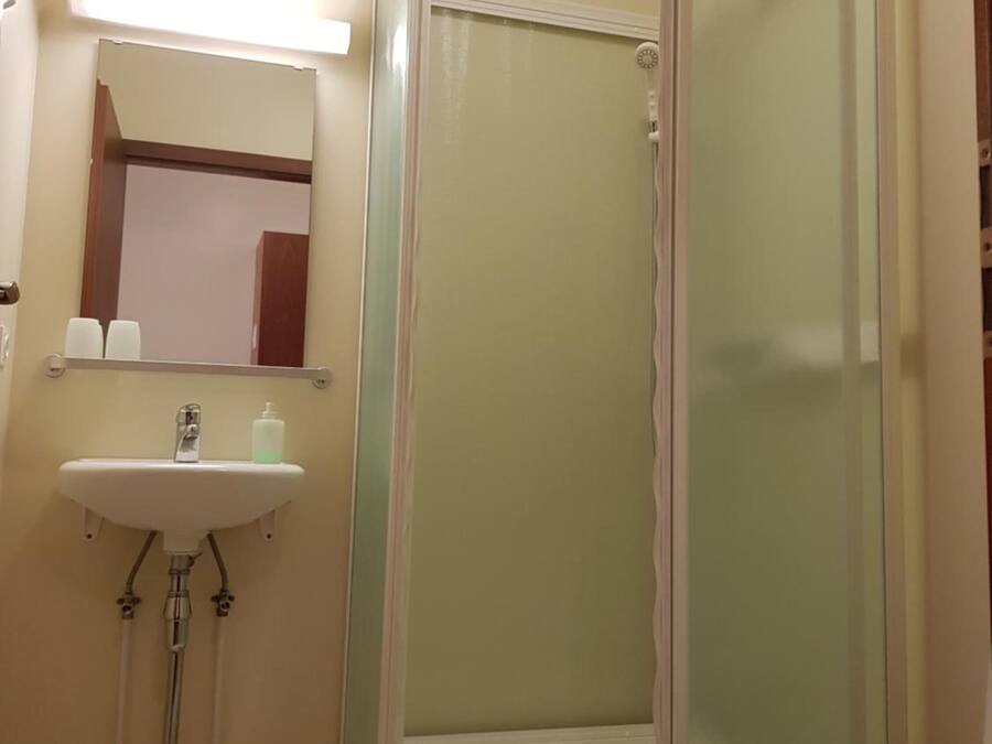 A bathroom with a glass-enclosed shower, a sink with a soap dispenser, and a toilet.