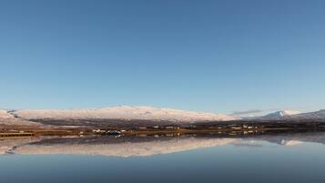 A calm lake reflecting snow-covered mountains and a small settlement with buildings along the shore.