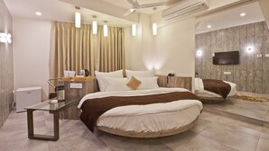 A modern bedroom with a large bed, a glass table, a ceiling fan, and a mounted TV. - Scenaria Hotel (Ahmedabad)
