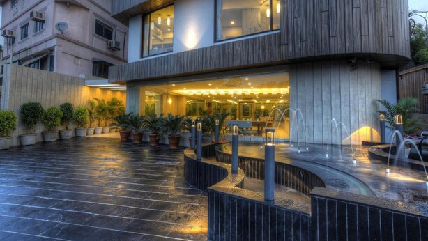 A modern hotel with a curved facade, outdoor seating area with potted plants, and a fountain. - Scenaria Hotel (Ahmedabad)