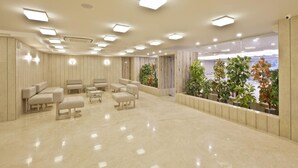 A spacious, well-lit lobby with a marble floor, seating area with sofas and armchairs, and a view of greenery through large windows. - Scenaria Hotel (Ahmedabad)