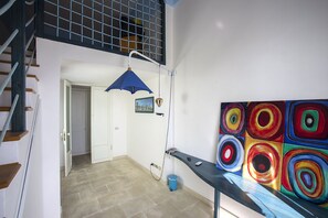 Eine Treppe führt zu einem Balkon, eine blaue Hängeleuchte, ein farbenfrohes abstraktes Gemälde und eine Tür zu einem anderen Raum.