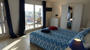Une chambre à coucher comprenant un lit, une armoire, un téléviseur et un balcon avec une chaise.