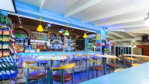 Eine Bar mit mehreren Tischen und Stühlen, Regalen voller Snacks und Getränke sowie einer Theke mit einer Registrierkasse.
