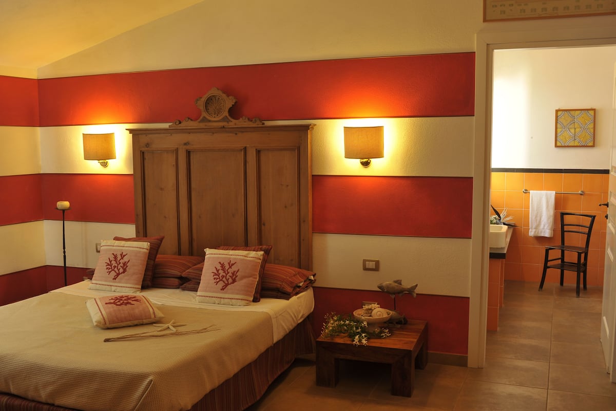 Ein Hotelzimmer mit einem Bett, Nachttischlampen, einem hölzernen Kopfteil und einem kleinen Tisch mit einer Vase.