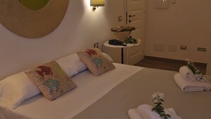 A hotel room with a bed, pillows, a bedside table, and a towel rack. - Hotel Villa Pimpina (Carloforte)