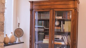 A corner with a wooden bookcase filled with books, two patterned chairs, a decorative vase, and a wall-mounted mirror. - Hotel Villa Pimpina (Carloforte)