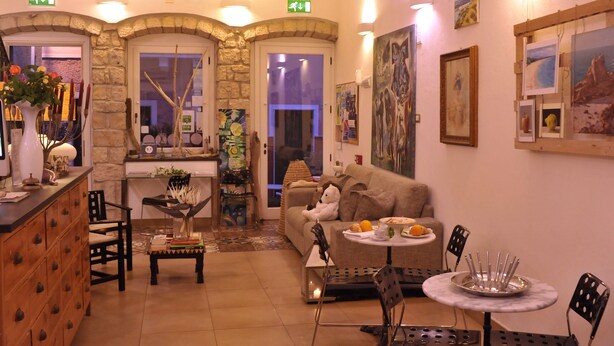 A cozy hotel lobby with a stone archway, a reception desk, a sofa, a dining table, and various artworks on the walls. - Hotel Villa Pimpina (Carloforte)