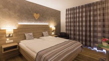 A hotel room with a large bed, bedside lamps, a heart-shaped wall decoration, and a view of the outdoors through curtains.