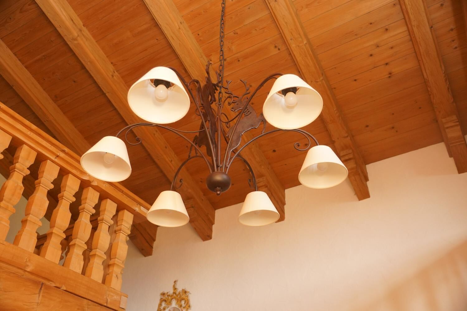 Un plafond en bois surmonté d’un lustre doté de plusieurs abat-jours blancs.