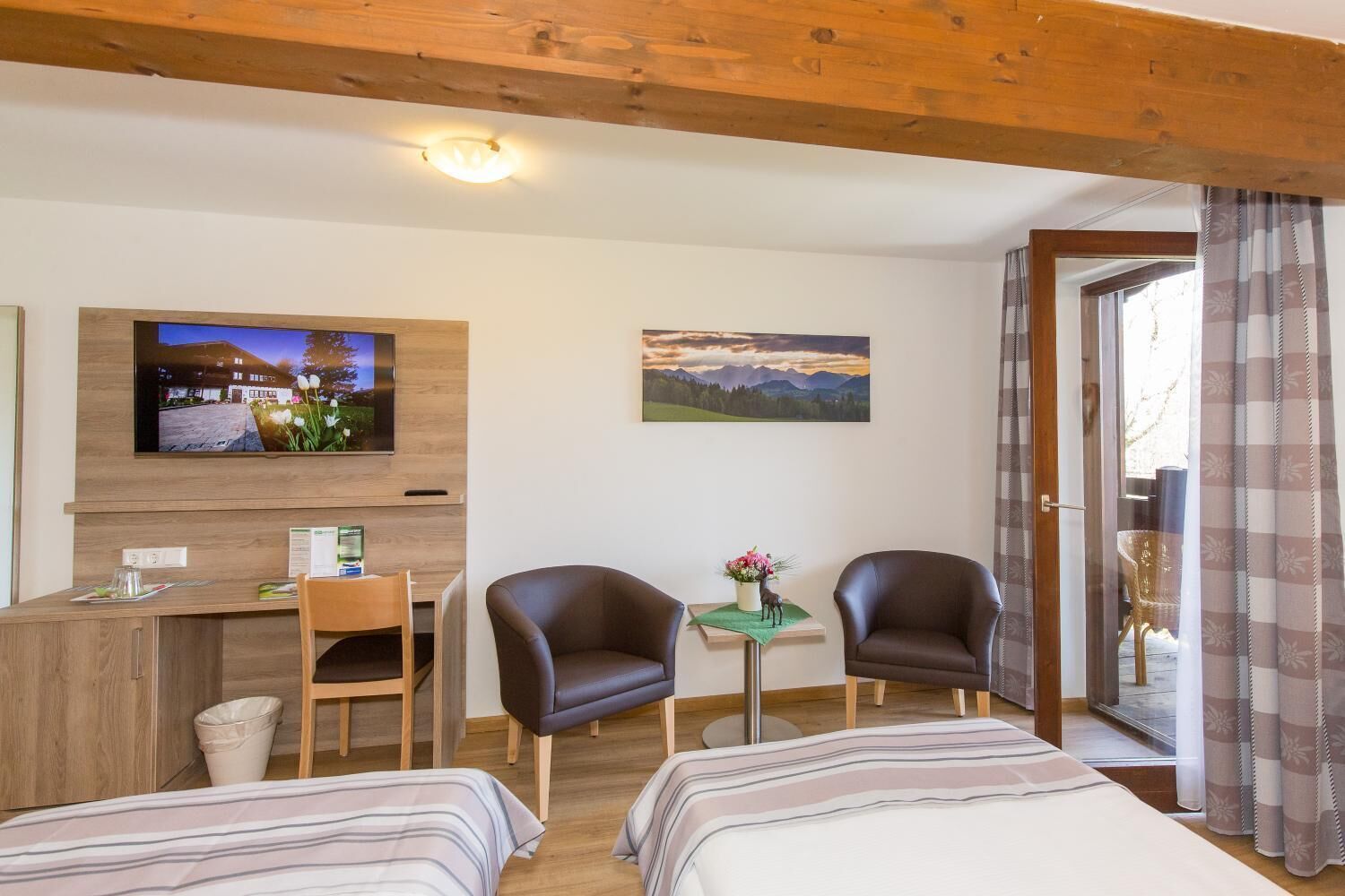 Ein Hotelzimmer mit Bett, zwei Stühlen, einem Schreibtisch, einem Fernseher und einem kleinen Tisch mit Blumenvase.