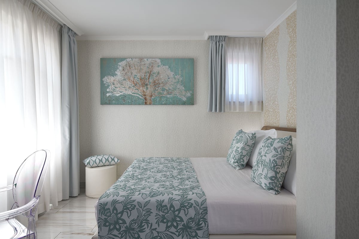Una camera da letto con un letto, una sedia, un tavolino e un quadro appeso al muro.