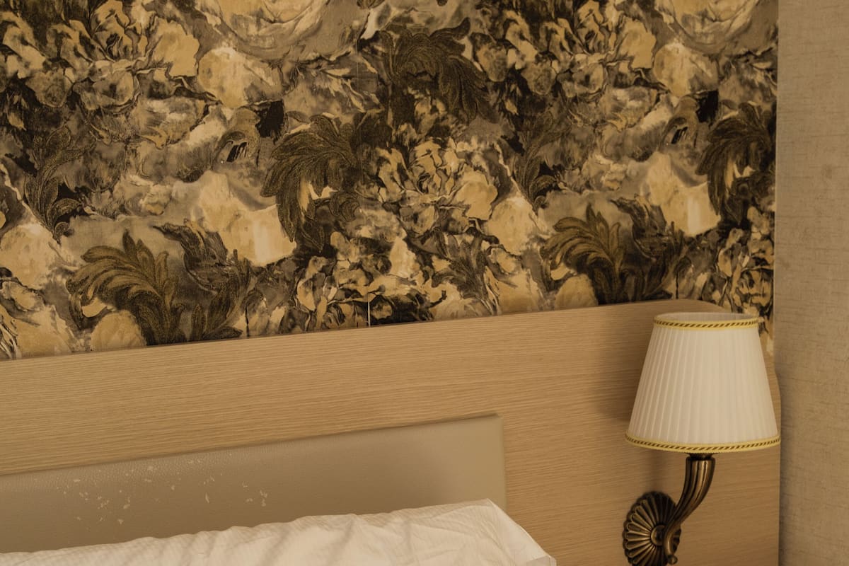 Un letto con lenzuola bianche, un comodino con una lampada e carta da parati a motivi floreali.