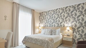 Une chambre d’hôtel avec un grand lit, une table de chevet avec une lampe, une chaise et une vue sur l’extérieur par une fenêtre avec des rideaux.