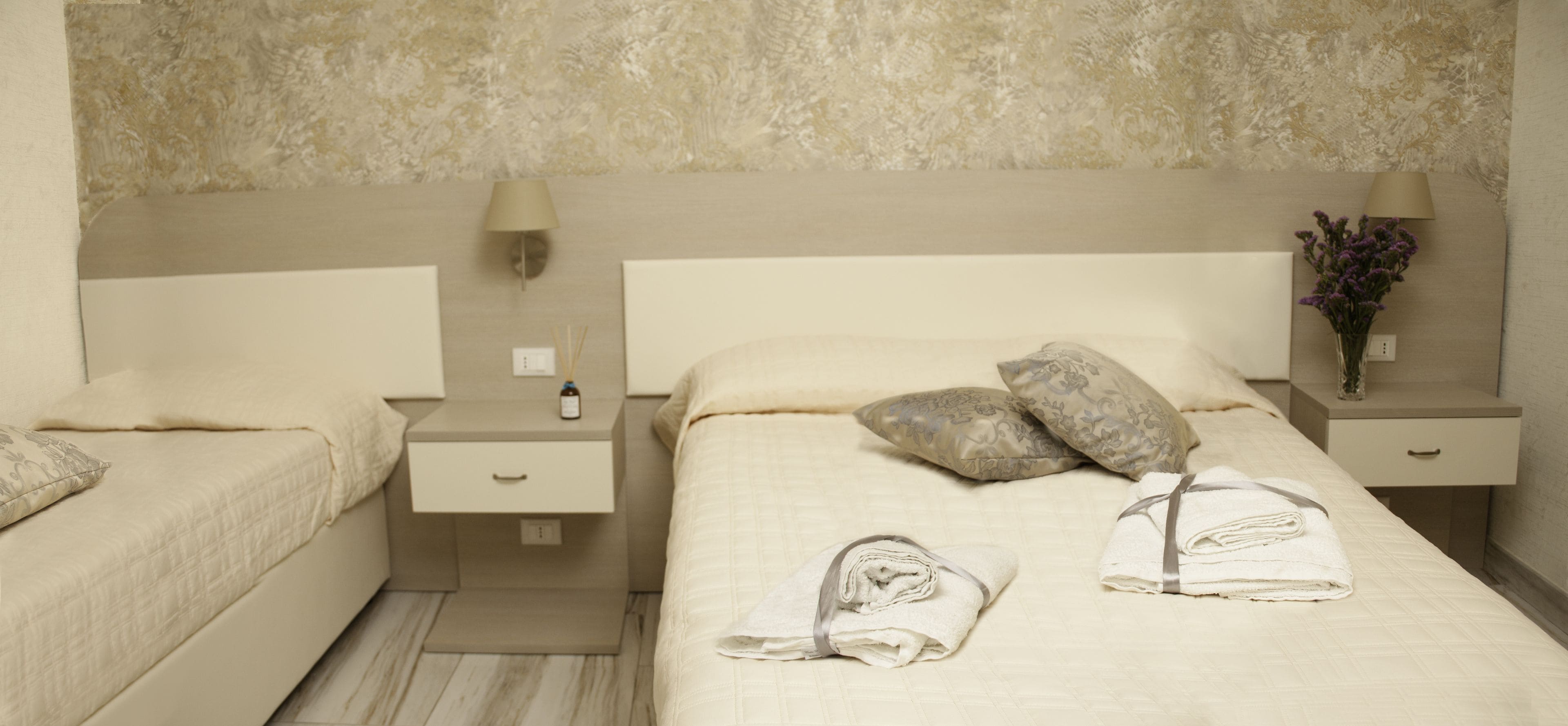 Una habitación de hotel con una cama grande, dos mesitas de noche, una lámpara y un jarrón con flores.