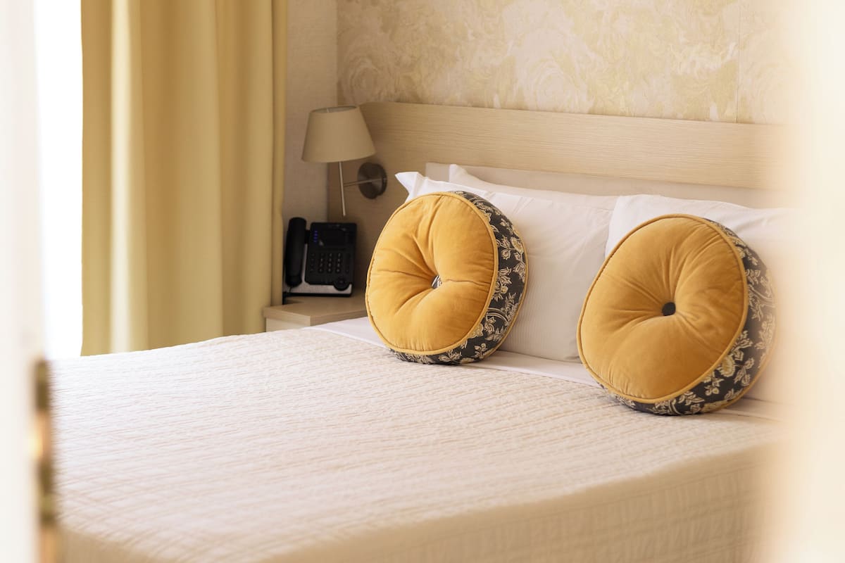 Un letto rifatto con due cuscini decorativi, una lampada da comodino e un telefono.