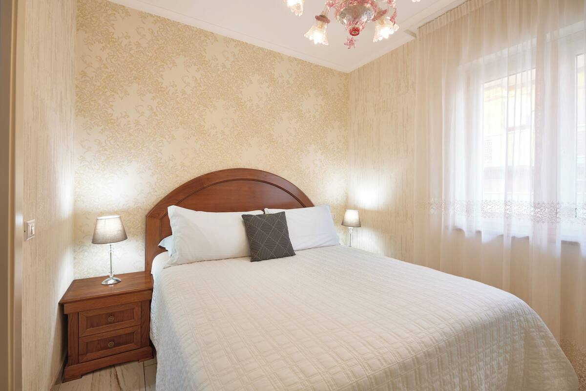 Un letto ben rifatto con una testiera in legno, due abat-jour e un comodino con lampada.