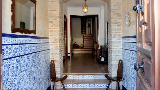 A hallway with blue and white patterned tiles, a wooden chair, and a staircase leading to another room. - Apartamentos Turísticos La Vida De Antes (Consuegra)