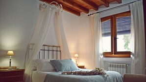 A bedroom with a four-poster bed, a nightstand, a lamp, and a window with curtains. - Apartamentos Turísticos La Vida De Antes (Consuegra)