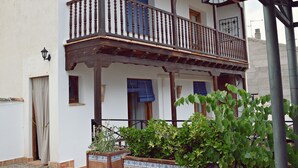 A two-story building with a wooden balcony, a door, and a window with blue shutters. - Apartamentos Turísticos La Vida De Antes (Consuegra)