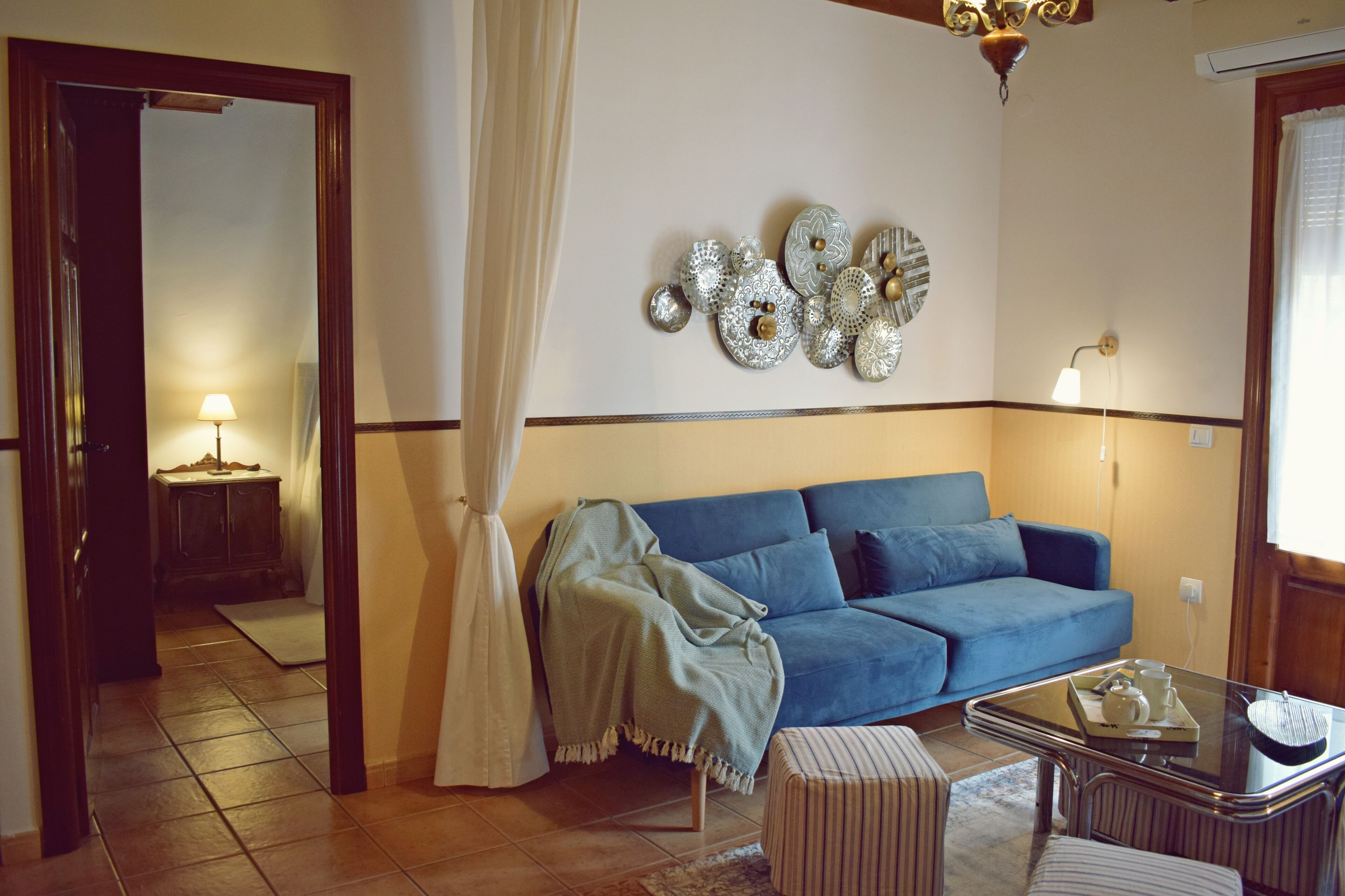 A living room with a blue sofa, a glass coffee table, and a decorative wall piece.