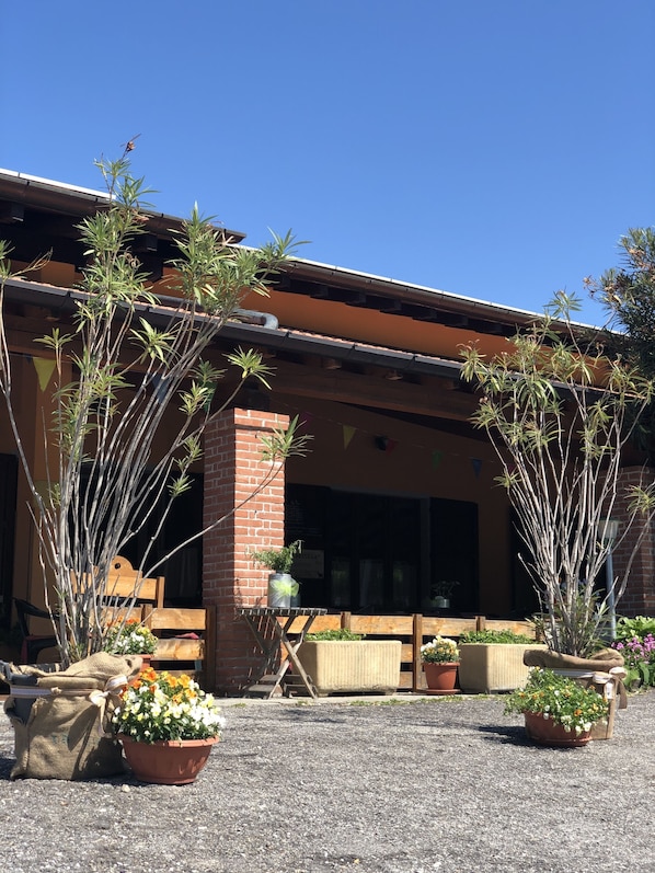 A building with a brick facade, a covered patio area with potted plants, and a clear blue sky.