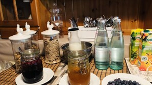 Una mesa de desayuno con diversos alimentos y bebidas, incluyendo botes de avena, una jarra de leche, botellas de agua y un plato de arándanos.