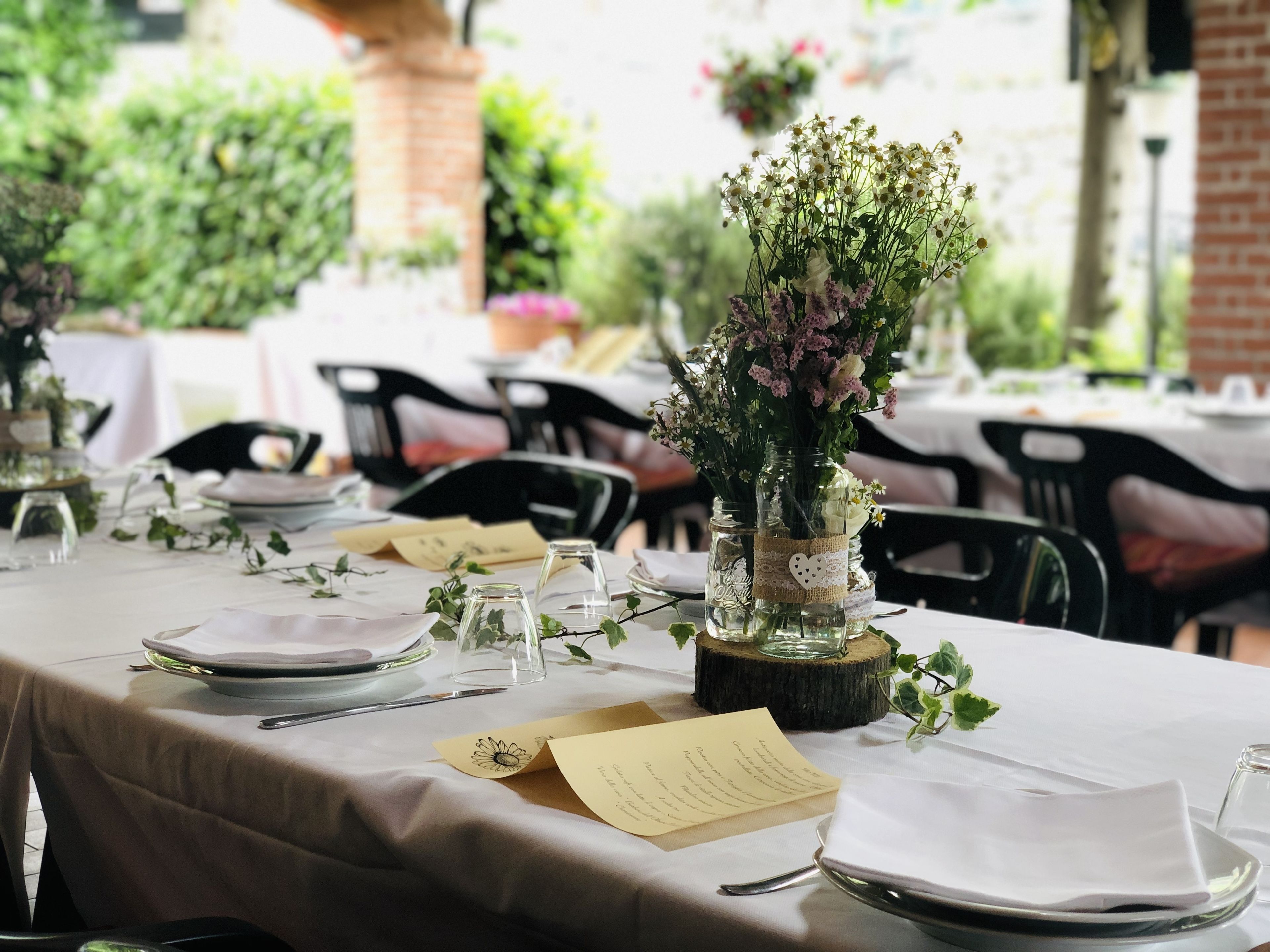 Une table mise pour un repas, avec un menu, un vase rempli de fleurs et un élément décoratif central en bois rustique.