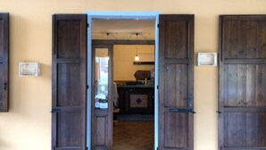 Una habitación con puerta de madera, una ventana pequeña y una cocina visible a través de la puerta.