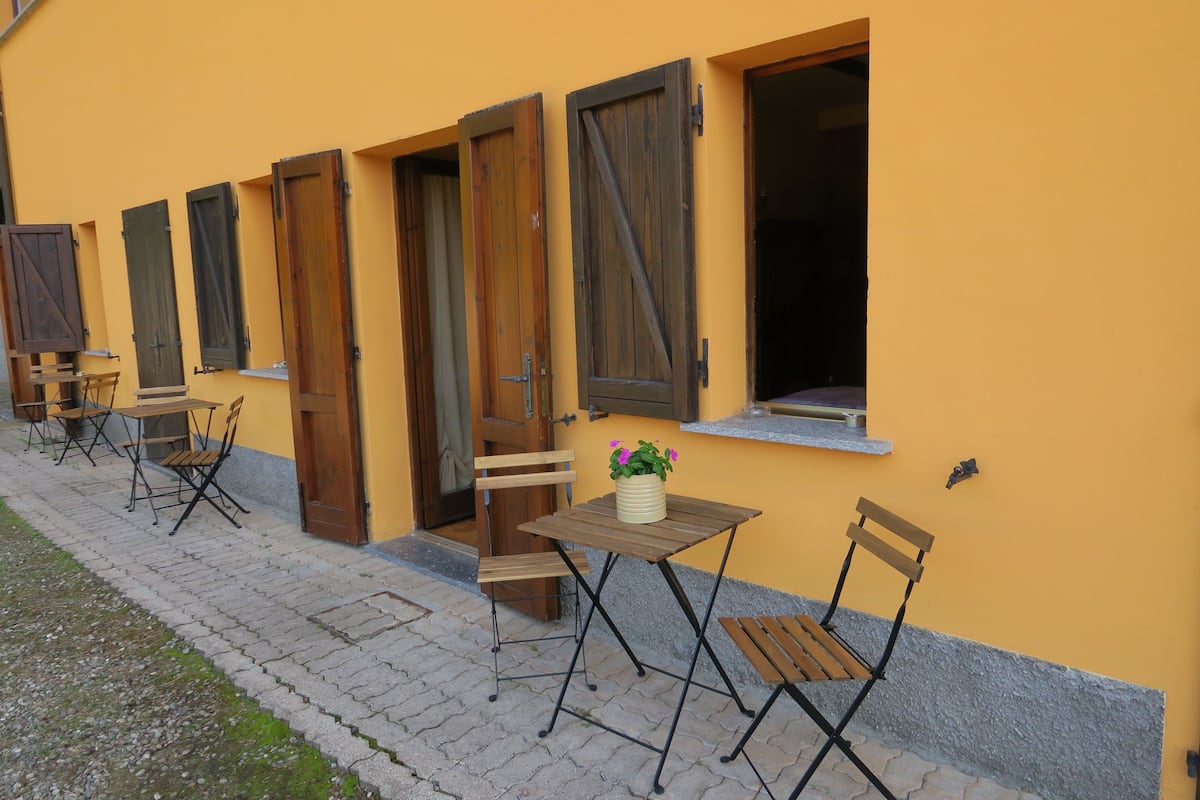 Ein gelbes Gebäude mit Holztüren und -fenstern, ein kleiner Tisch mit einem Blumentopf und Sitzgelegenheiten mit Stühlen und Tischen im Freien.